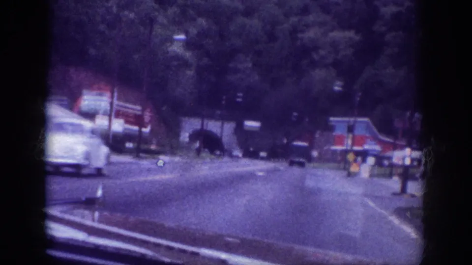 Early 1960s automobile in heavy motion blur on a Memphis, Tennessee roadway circa 1963, roadside commercial strip visible, filmed on aged 8mm stock.