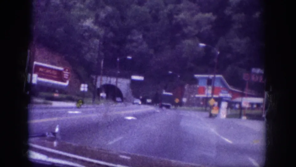 Stone-arch tunnel approach on a Memphis, Tennessee roadway circa 1963, with commercial roadside signage and tree-lined corridor visible on aged 8mm film.