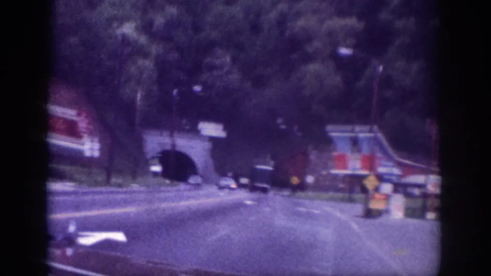 Stone tunnel portal and roadside billboard signage along a Memphis, Tennessee road circa 1963, shot from a moving vehicle on 8mm film.