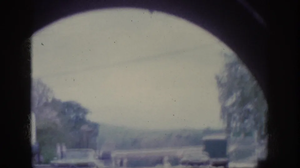POV shot emerging from a tunnel on 8mm circa 1963, with the concrete arch overhead and a tree-lined road opening into washed daylight.
