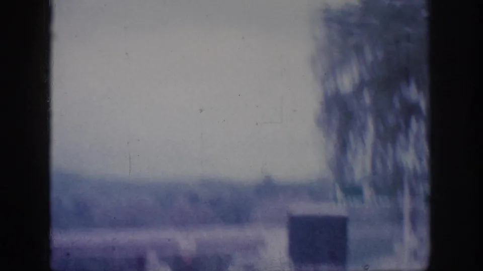 Post-tunnel road scene on 8mm circa 1963, showing a tree-lined road under an overcast sky with heavy blue-grey colour fade typical of aged 8mm film.