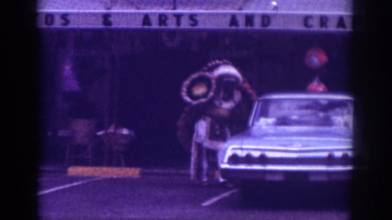 8mm home movie circa 1963, Memphis area: costumed figure with elaborate feathered headdress beside a classic American car, partial commercial signage overhead, strong purple film shift.