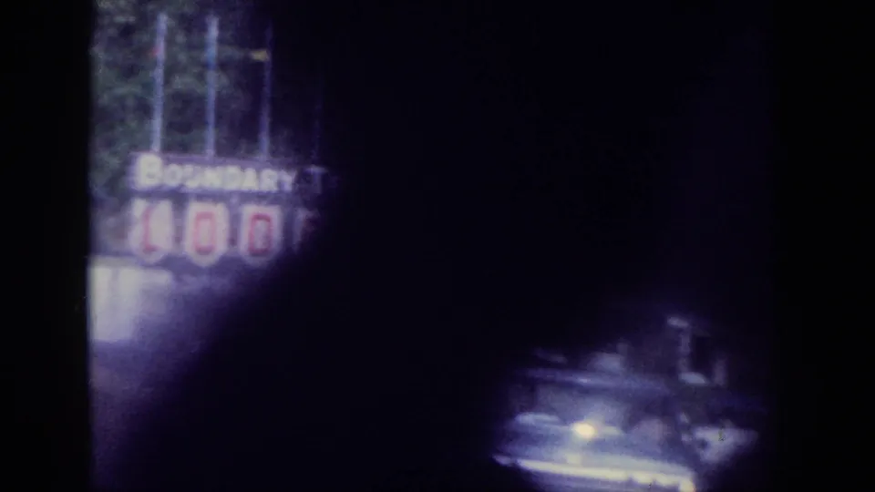 Opening frame of a 1963 8mm home movie; heavily underexposed road scene with a partially legible 'BOUNDARY' sign visible at left, filmed through a car windshield.