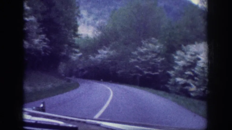 Closing frame of a 1963 8mm road-trip clip; winding road through spring foliage consistent with rural Tennessee scenery, with blue-purple color cast from aged 8mm stock.