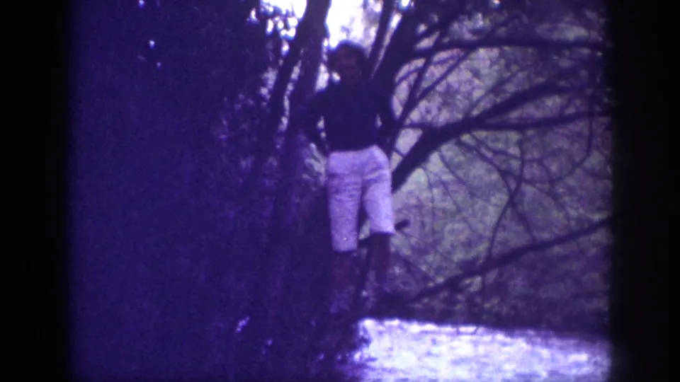Adult male near a small stream among bare deciduous trees; 8mm home movie from Memphis, Tennessee, 1963, with pronounced violet dye shift.