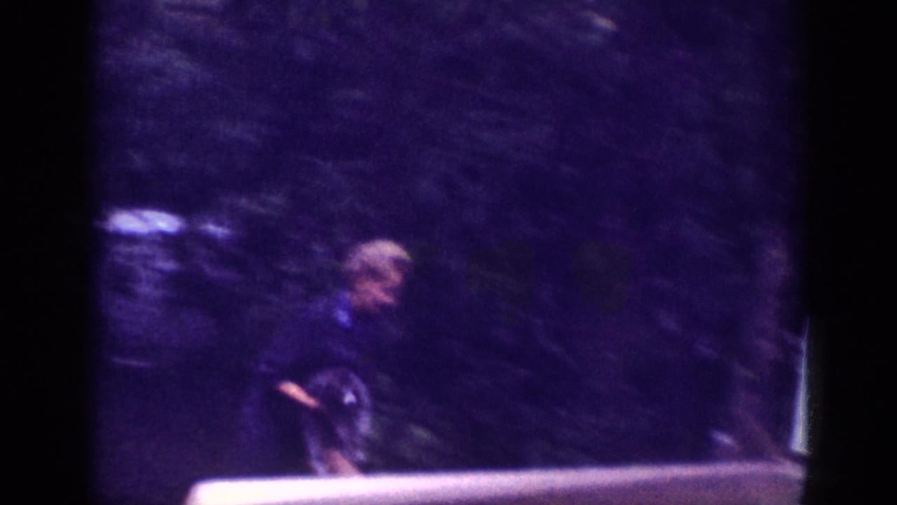 Woman in a dark coat walking through a wooded roadside in what appears to be early-1960s 8mm home movie footage, possibly Memphis, Tennessee, 1963.