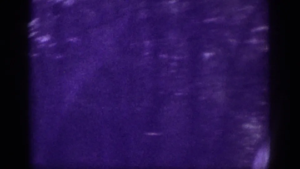 8mm home movie frame circa 1963, extreme purple dye-shift obscures most detail; faint tree silhouettes and a light road strip remain visible at lower edge.
