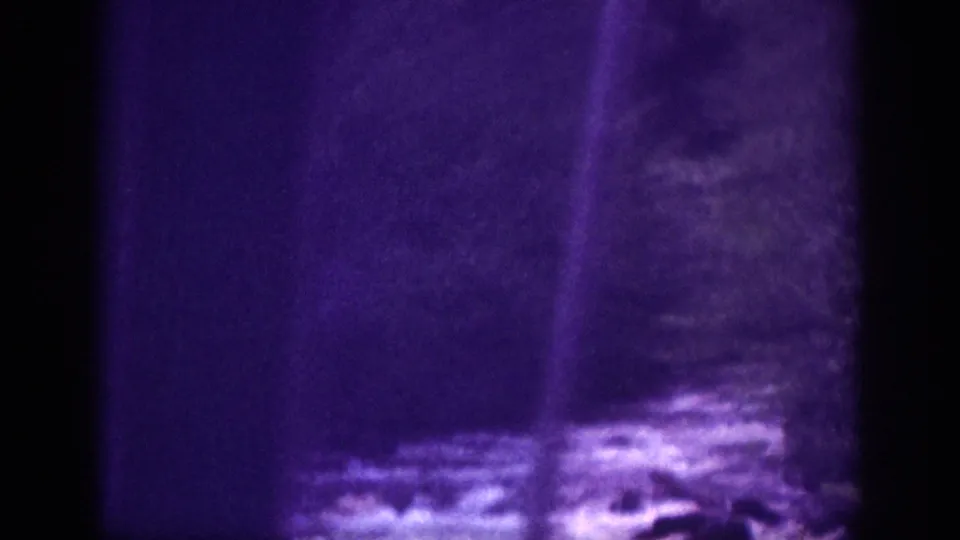 River crossing view from moving vehicle, circa 1963 Memphis area; rocky water, forested bank, vertical film light-leak streaks, and purple dye-shift on aged 8mm stock.