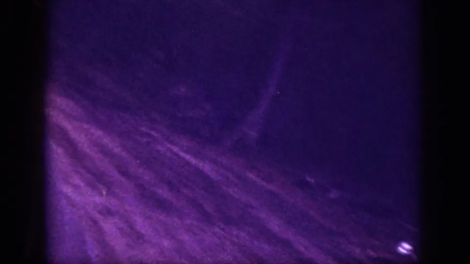 Opening frame of 1963 8mm night shot, Memphis area — deep violet color cast, surface scratches, and a faint light point visible against dark ground.