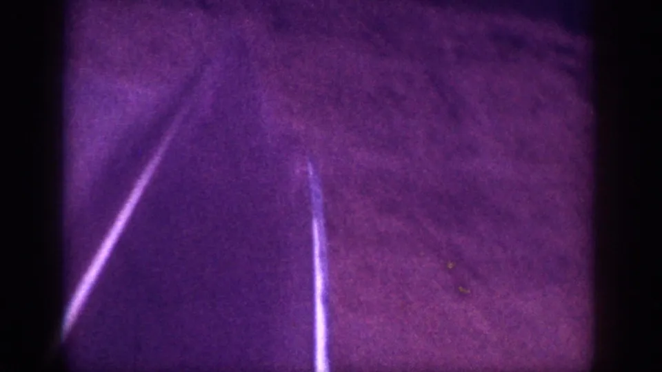8mm night frame, c.1963, Memphis area — diagonal bright line (possibly road edge or headlight trail) over textured dirt ground, mauve-purple color cast.