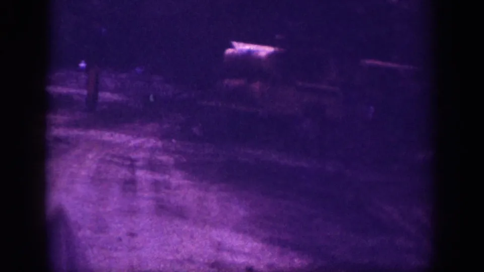 Second frame from a 1963 8mm clip attributed to Memphis, Tennessee; a light-colored unidentified object sits on dark ground under heavy purple dye-layer distortion.