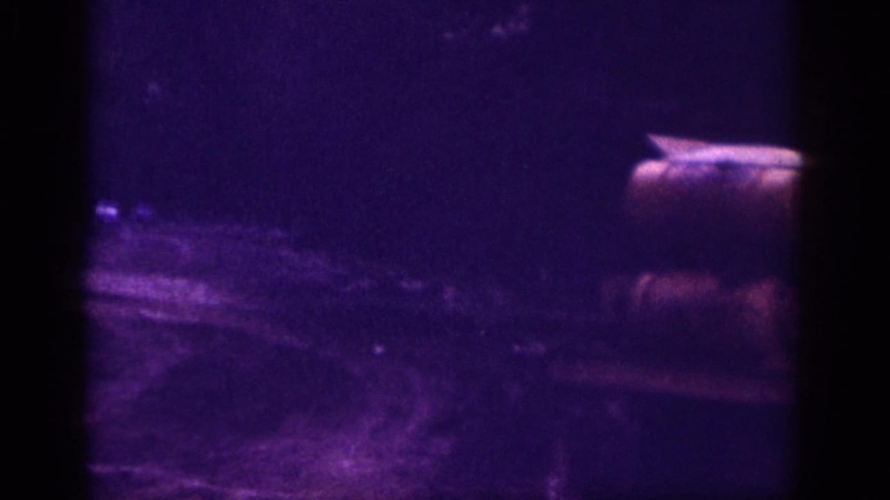 Partial rear view of a car on a dirt road, Memphis Tennessee area circa 1963, on aged 8mm color film with strong violet dye shift and coarse grain.