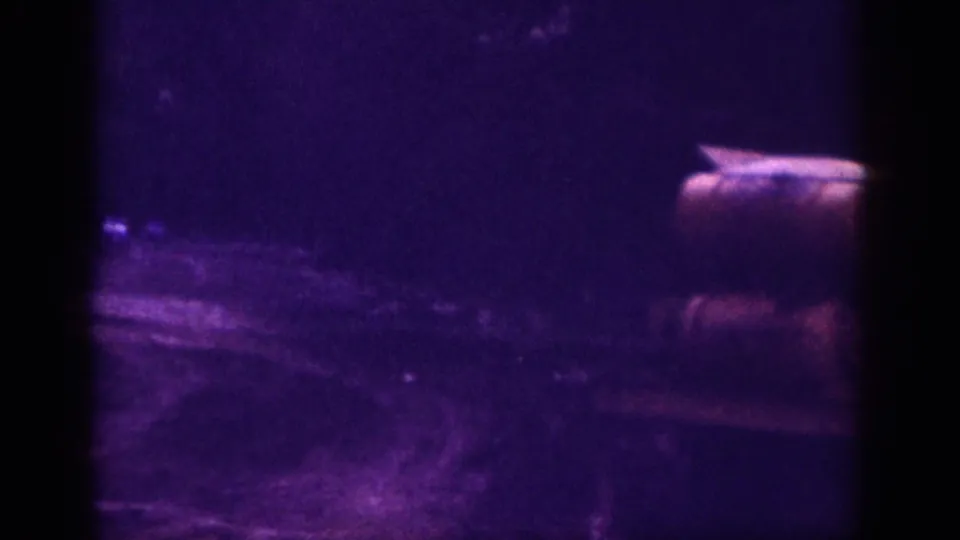 Partial rear view of a car on a dirt road, Memphis Tennessee area circa 1963, on aged 8mm color film with strong violet dye shift and coarse grain.