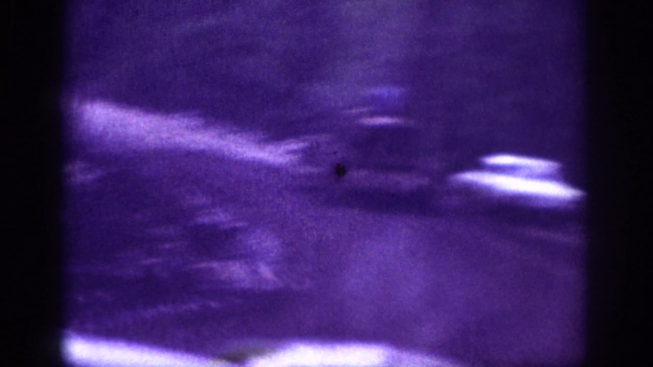 Heavily motion-blurred 8mm frame showing faint vehicle shapes on a road, strong purple color cast.