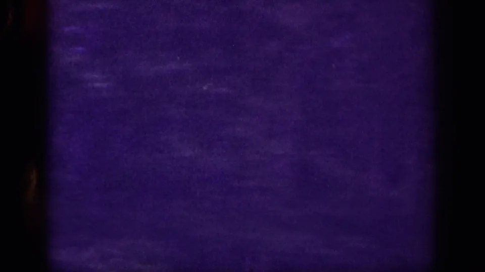 Transitional 8mm frame in near-blackout with a faint amber edge trace — likely a brief exposure gap or in-camera splice during the mountain drive.