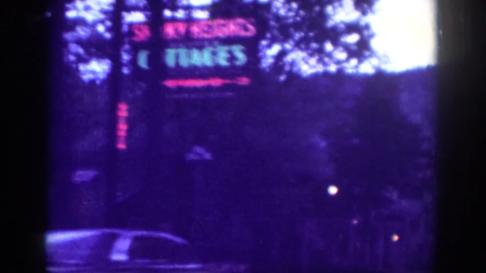 Close-passing neon sign for a roadside cottages motel, full text partially obscured, shot from a car window on an 8mm Tennessee road trip, circa 1963.
