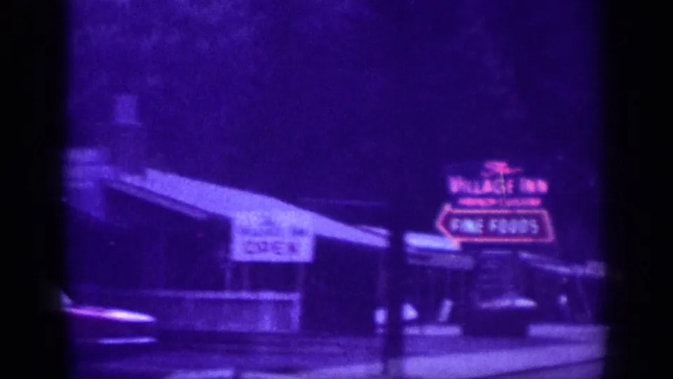 Roadside neon sign for The Village Inn advertising Fine Foods and Open, captured on 8mm from a passing car in what the metadata identifies as Tennessee, circa 1963.