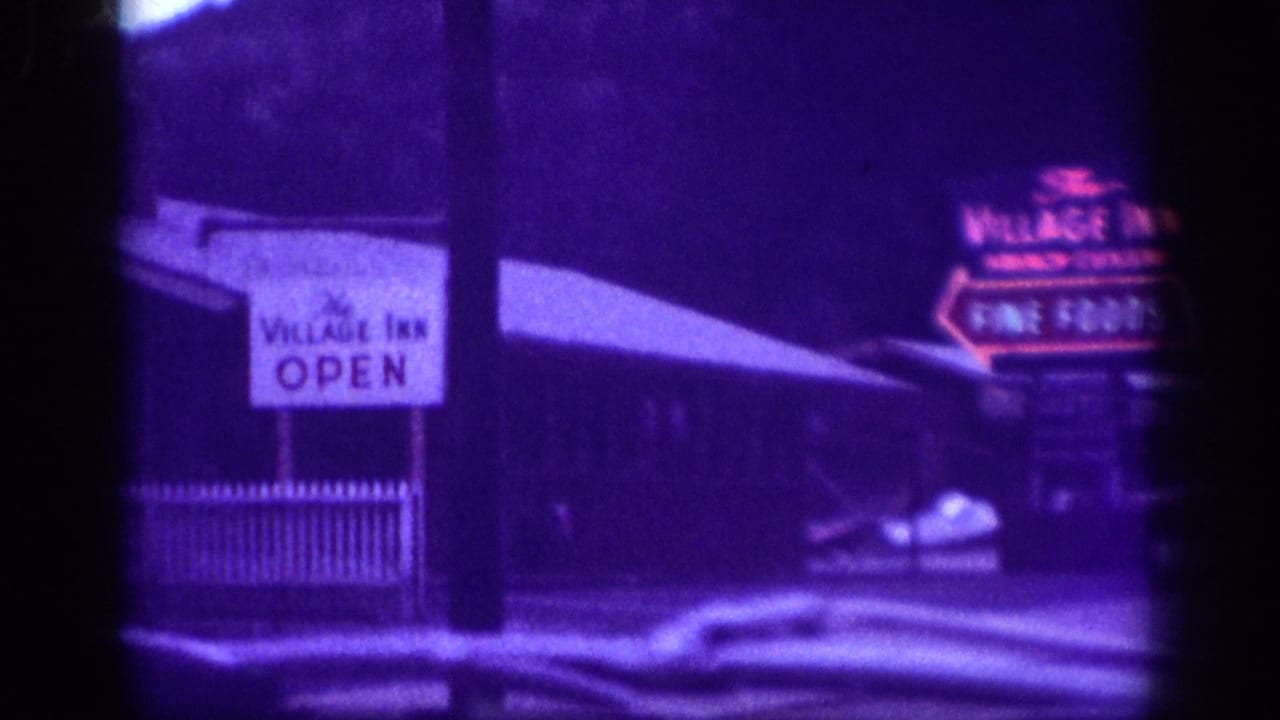 1963 Memphis-area home-movie frame showing a roadside building, an Open sign, and a glowing Village Inn sign for French cuisine and fine foods, partly obscured by dark frame edges.