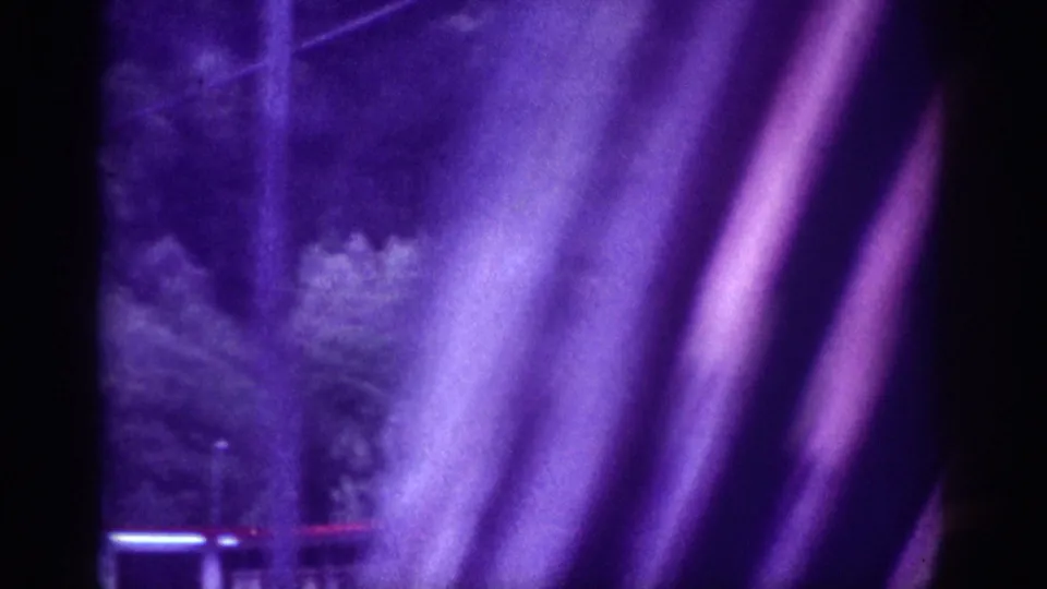 8mm motion-blur frame from a 1963 Memphis night drive showing streaking artificial light trails and blurred roadside foliage under a strong purple cast.