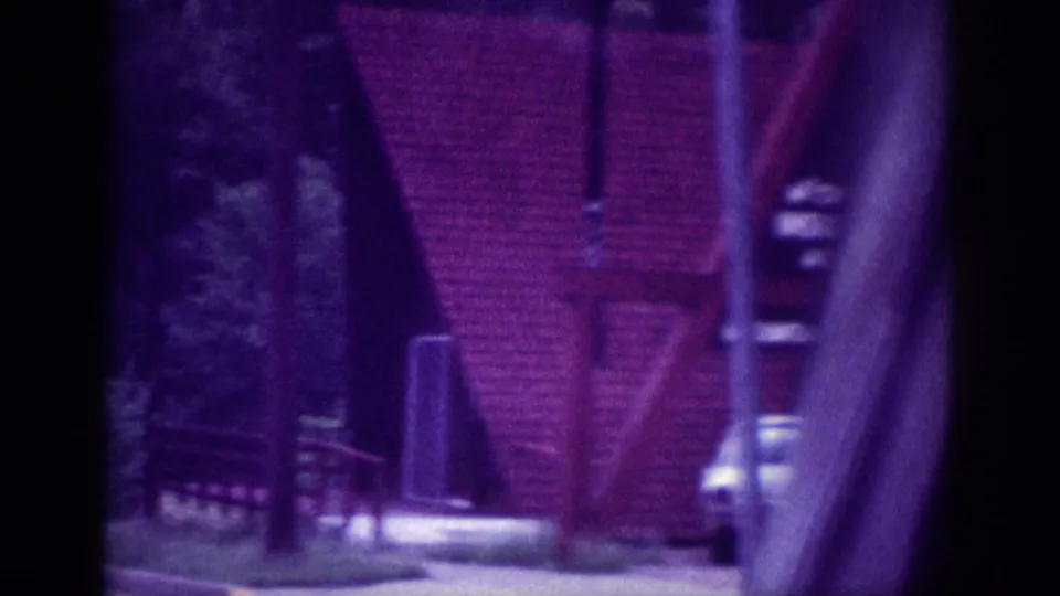 Drive-by 8mm view of a distinctive A-frame structure in Memphis, 1963, with trees, utility pole, and a light-colored car alongside.