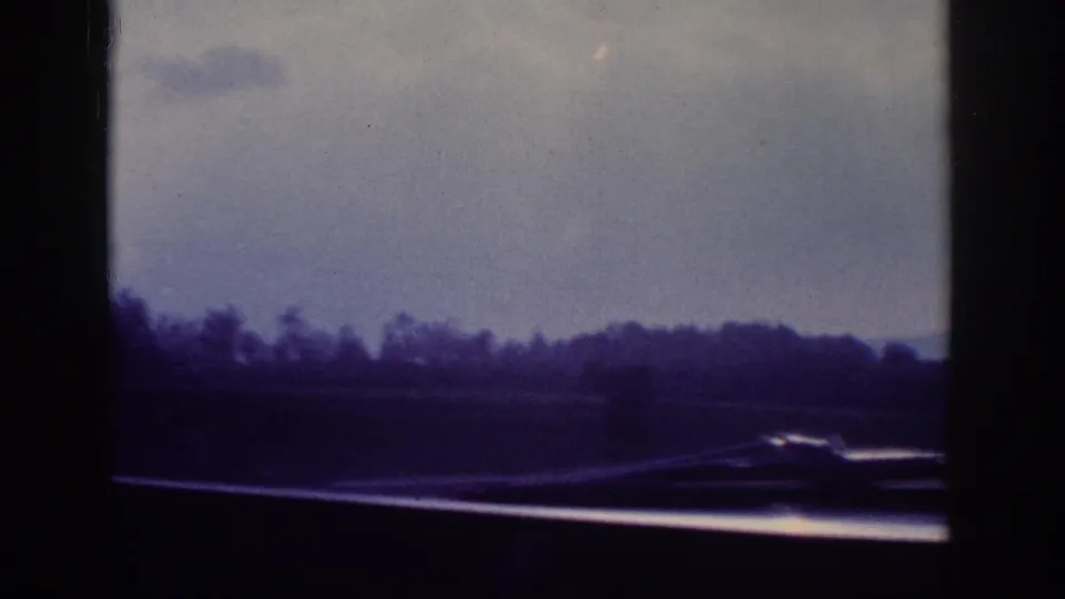 Flat rural landscape with a tree line and highway, filmed through a car window; 8mm road-trip footage consistent with 1963 American travel.