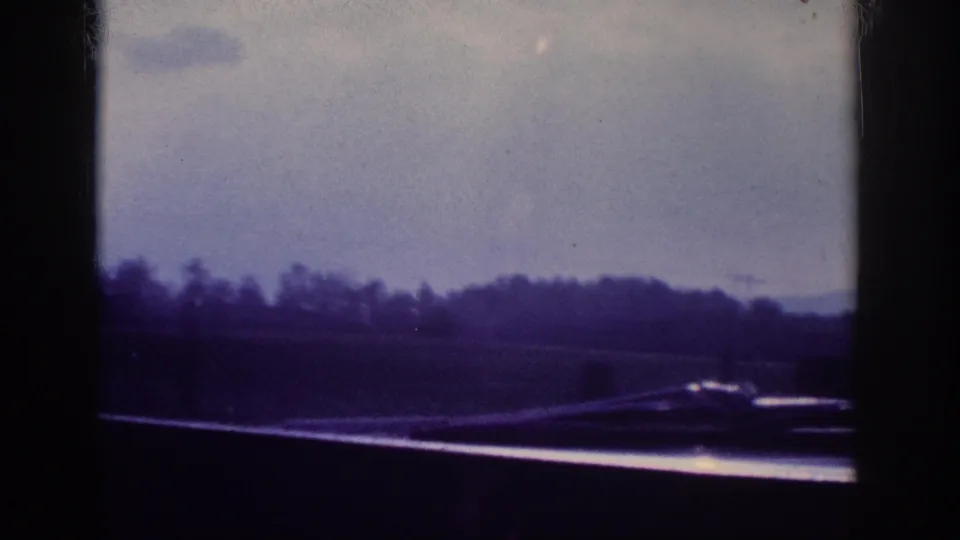Through-windshield view of a US highway bordered by dense trees, 8mm home movie footage attributed to Tennessee circa 1963.