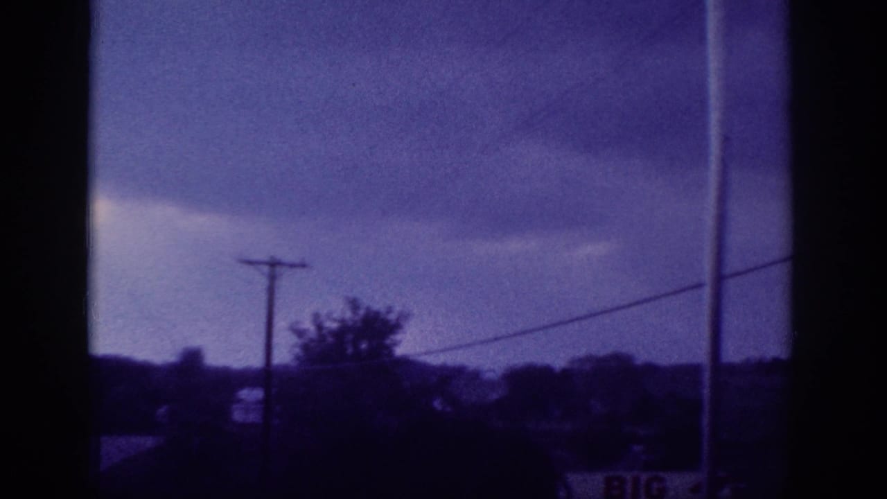 8mm frame showing a stormy blue-purple sky with a utility pole, power lines, and silhouetted trees, shot from a moving vehicle.