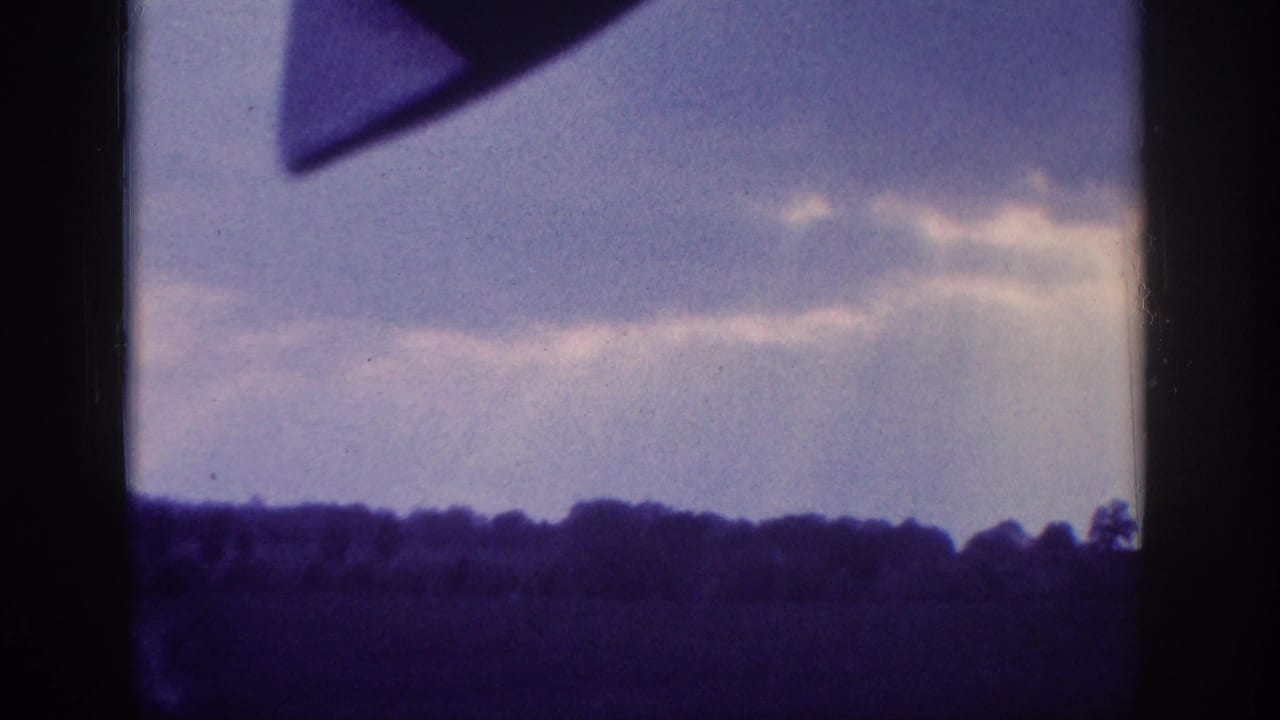 Aged 8mm home-movie frame circa 1963 showing layered clouds through a car window, with the vehicle's interior frame visible in the upper right corner.