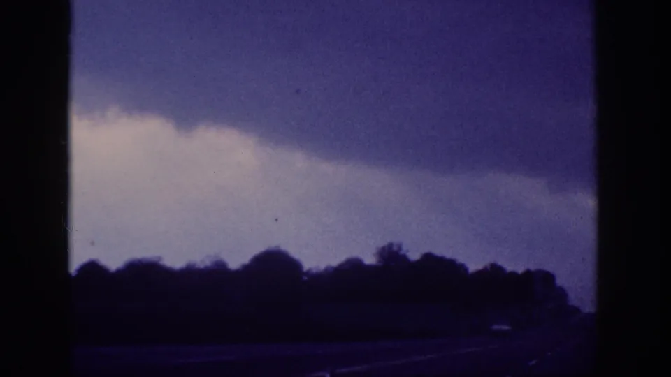 1963 8mm home movie — storm clouds shifting over a Tennessee treeline viewed from a moving vehicle's passenger seat, aged film color shift throughout.