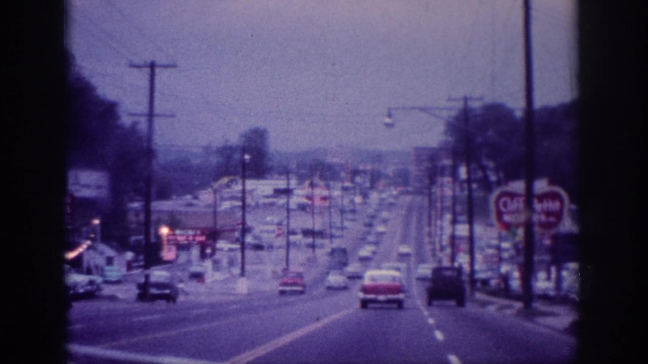 Multi-lane suburban road with cars, utility poles, and roadside signs.