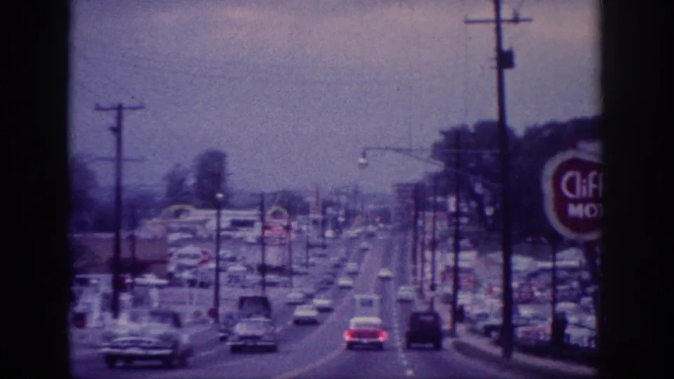 Memphis suburban driving footage shows cars on a broad commercial road, with utility poles, roadside businesses, a motel sign, and faded blue-purple 8mm color.