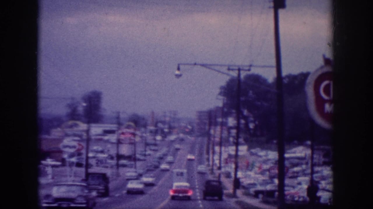 1963 Memphis-area home-movie frame looking forward along a multi-lane commercial road with classic cars, utility poles, and roadside business signs.