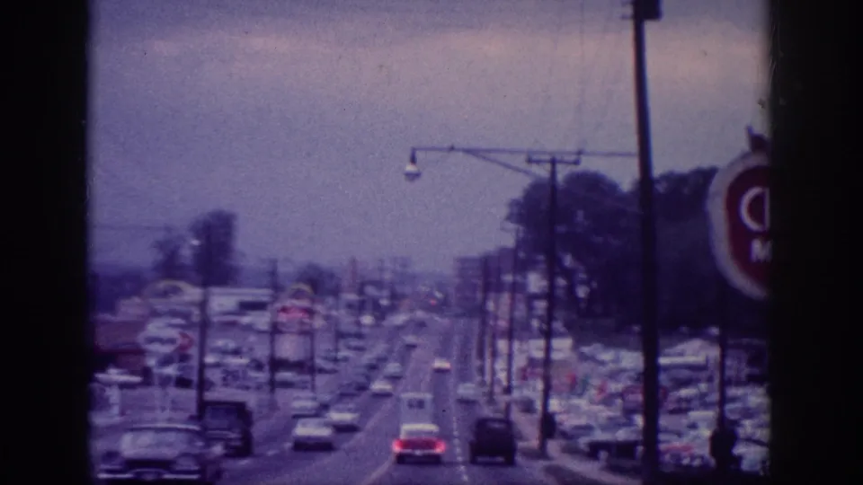1963 Memphis-area home-movie frame looking forward along a multi-lane commercial road with classic cars, utility poles, and roadside business signs.
