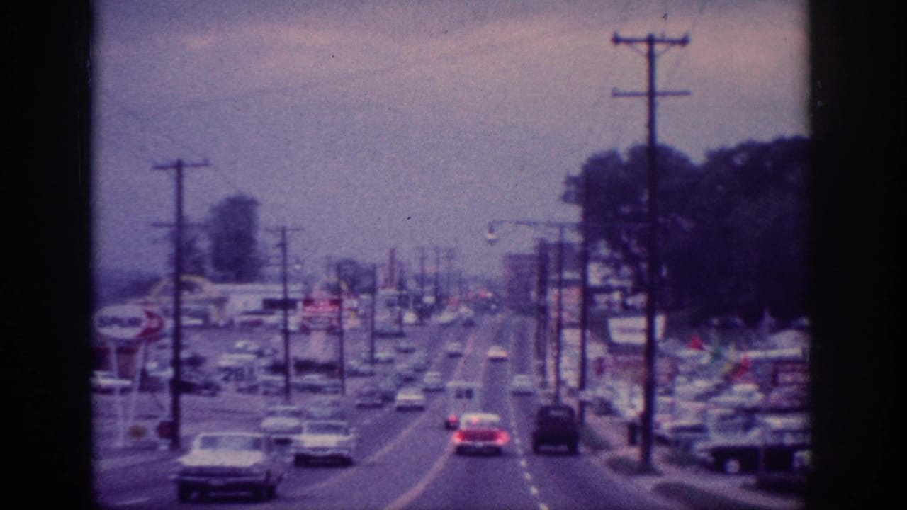 Cars travel along a divided roadway lined with utility poles and business signs.
