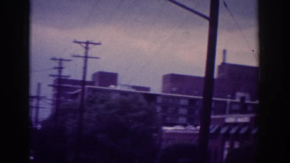 Late-frame 8mm view from a moving vehicle in Memphis, with utility poles, low commercial buildings, roadway signs, and blurred roadside vegetation.