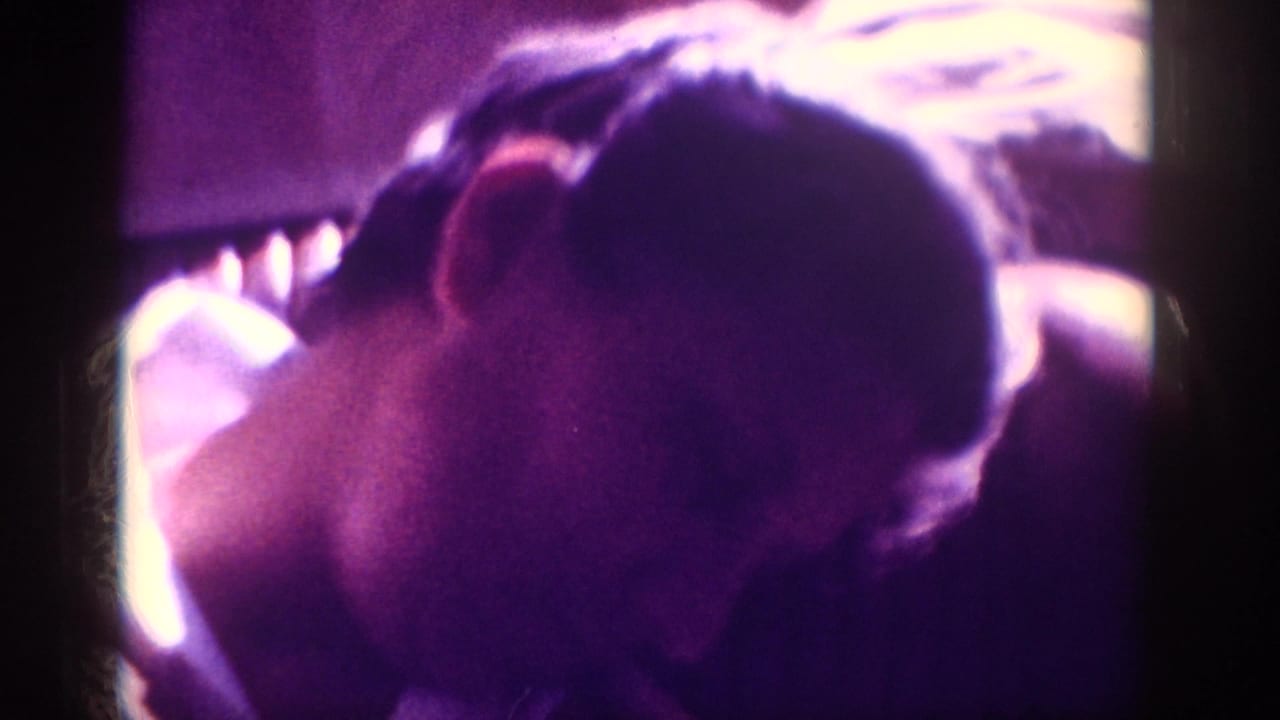 Top-down view of a man with dark hair, head bowed forward, in a heavily purple-cast 8mm home movie frame.