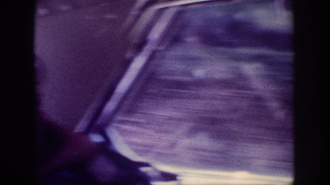 Motion-blurred 8mm home movie frame of a car interior in transit, circa 1963, with heavy purple color shift and indistinct seat detail.