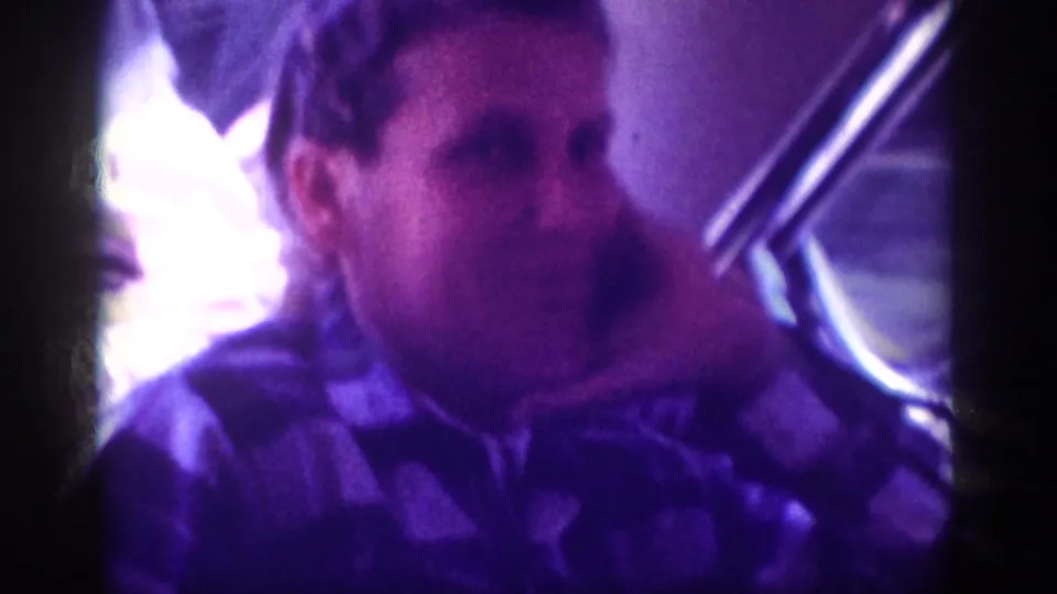 Young man in patterned shirt, possibly wearing a dark knit cap, photographed in a car backseat in an 8mm home movie circa 1963, Memphis, Tennessee.