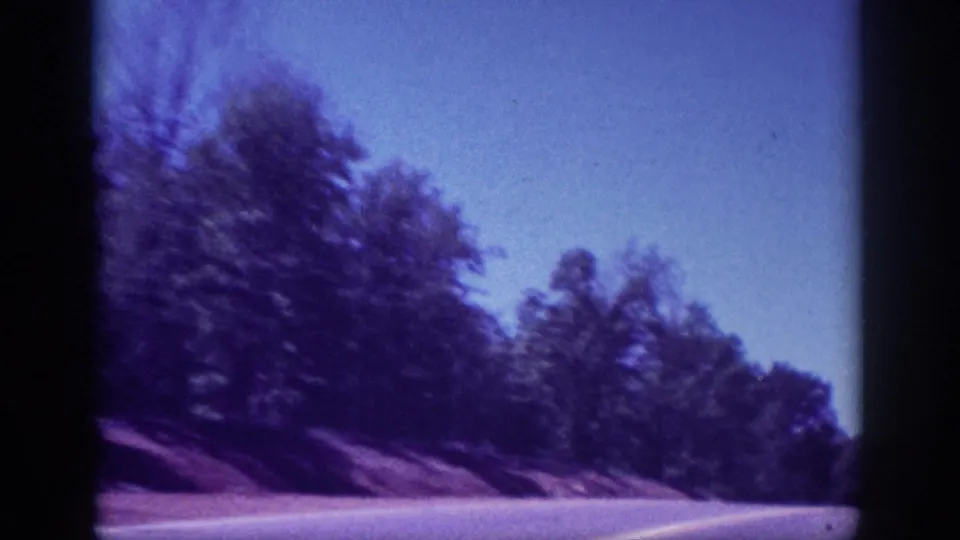 Through-windshield view of a winding two-lane road flanked by dense trees, shot on 8mm in the Memphis, Tennessee area, ca. 1963.