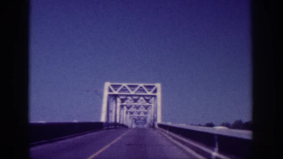 Close approach to a white steel lattice truss bridge on a two-lane road, ca. 1963, Memphis Tennessee area; shot on 8mm film.