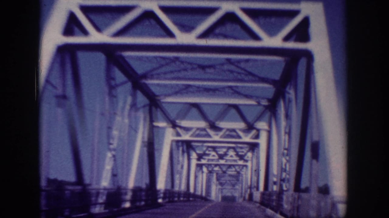 1963 Memphis vehicle POV passing beneath large white truss beams, with the bridge structure filling most of the frame.