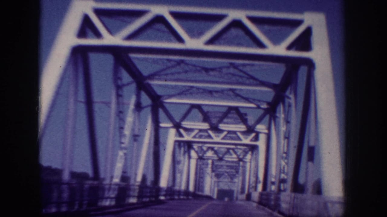 1963 Memphis vehicle POV continuing through the steel truss bridge, with repeating portals receding down the roadway.