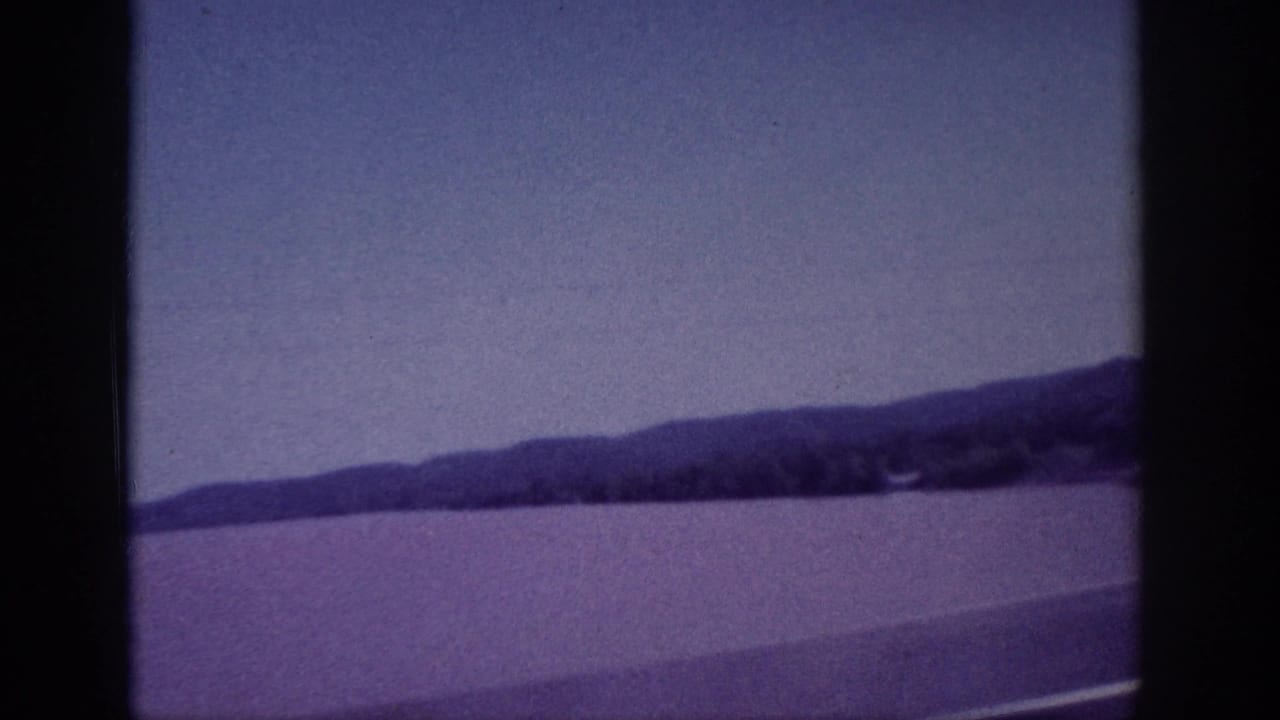Calm water with distant low hills under a purple-tinged sky, framed by dark film borders.