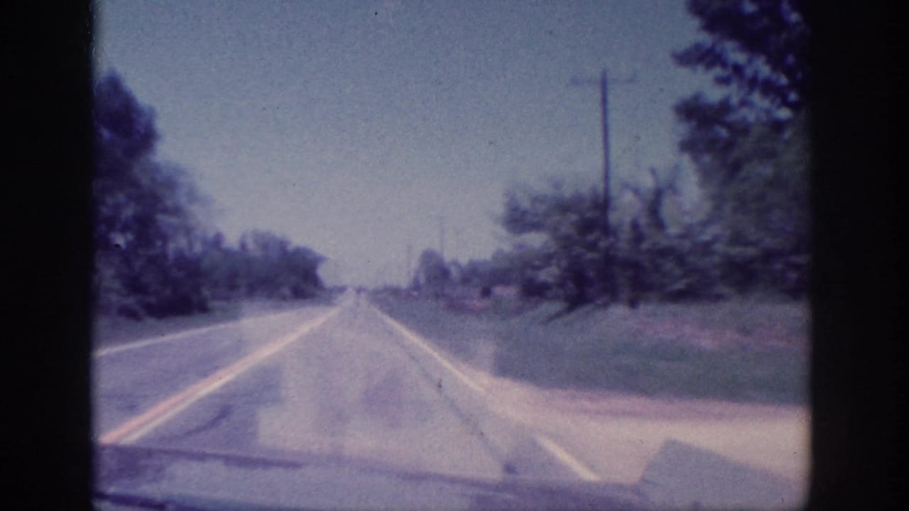 Two-lane rural road with double yellow lines, trees, grass shoulder, and utility poles ahead.