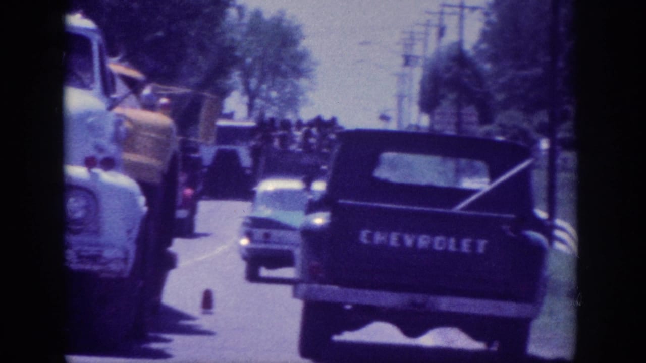 8mm home movie, Memphis Tennessee area, 1963 - rear view of a Chevrolet pickup truck tailgate in traffic, other vintage vehicles alongside, tree-lined road.