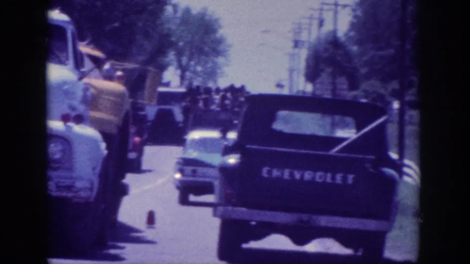 8mm home movie, Memphis Tennessee area, 1963 - rear view of a Chevrolet pickup truck tailgate in traffic, other vintage vehicles alongside, tree-lined road.