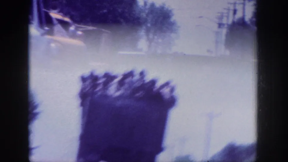 8mm in-camera transition - dark silhouetted figures smeared by motion blur against an overexposed pale sky, reflecting handheld instability from a moving vehicle.
