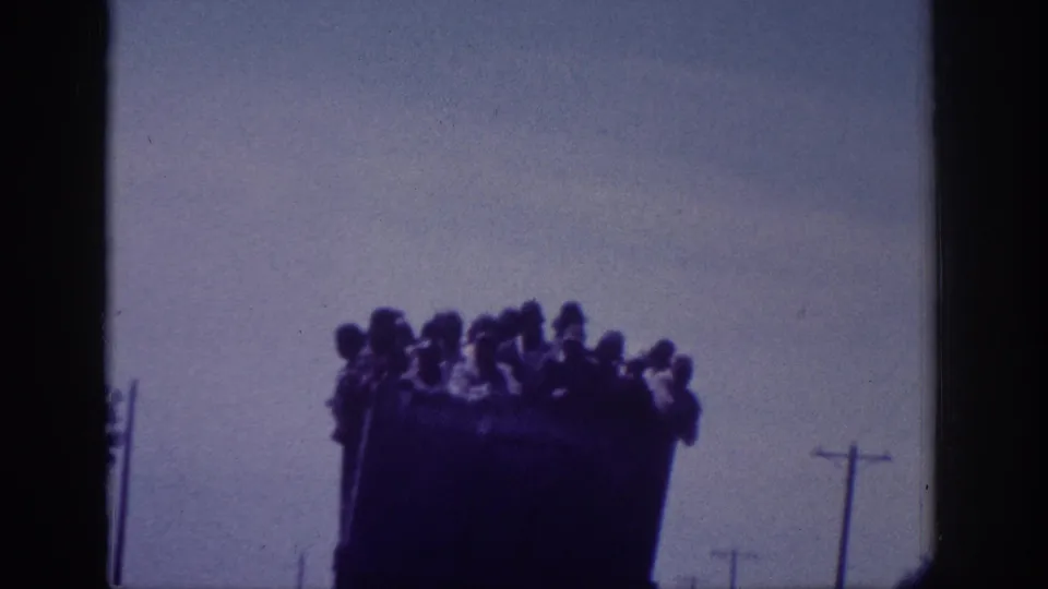 8mm home movie, Memphis area, 1963 - large dark truck with many people packed into the open bed, silhouetted against a pale sky, telephone poles in background.