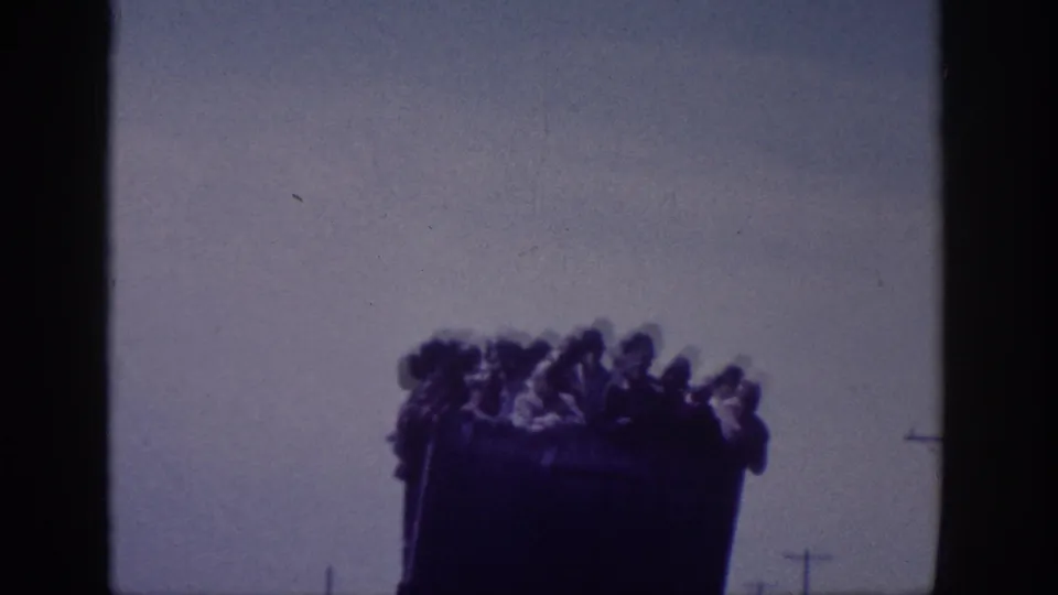 8mm home movie, Memphis area, 1963 - close rear view of a dark truck bed crowded with people in silhouette, hazy sky above, telephone poles to the right.