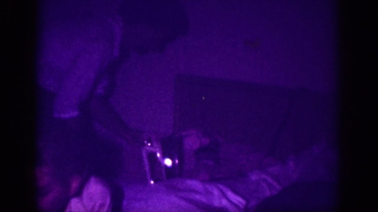 Purple-tinted 8mm frame with a partial figure in the upper area, a small bright light point at center, and draped fabric below.